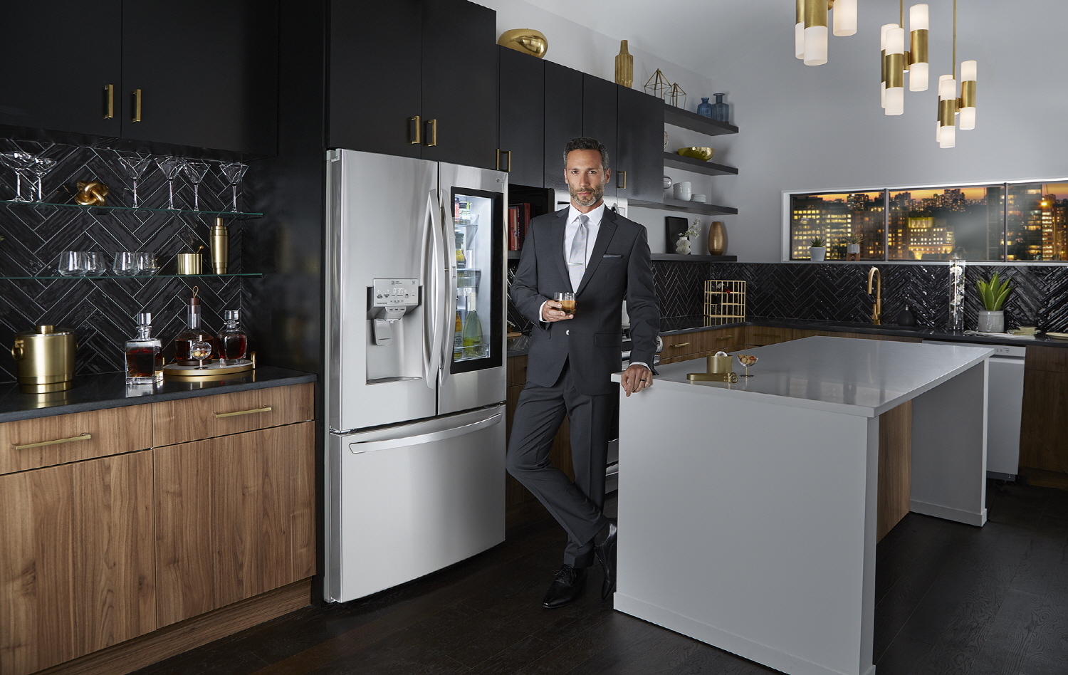 A man in suit standing in front of LG InstaView Door-in-Door™ refrigerator in a kitchen, holding a glass of beverage with Craft Ice™
