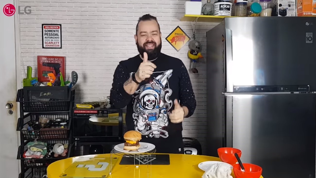 Filipe Nascimento smiles and gives a thumbs up with the burger he just made