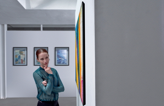 A side view of the LG GX Gallery series TV on display in a gallery with a woman looking at it with intrigue