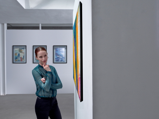 A side view of the LG GX Gallery series TV on display in a gallery with a woman looking at it with intrigue