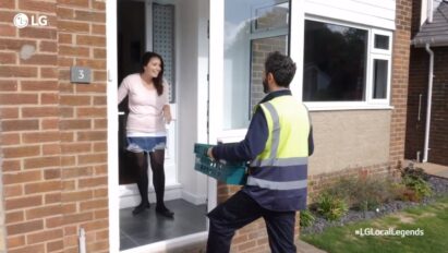 A woman looks overjoyed as a man pays a visit to her front door to gift a large box of groceries