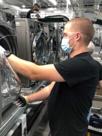 Another factory worker checking the quality of an LG washing machine's door