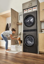 A woman gives her pet dog a shower next to a fitted LG WashTower in black