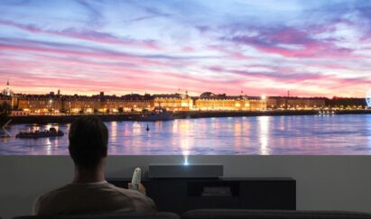 A man uses LG CineBeam to project a gigantic high-resolution image of a town by the sea on his living room wall