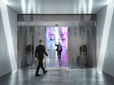 A man greeting a visitor through an opening transparent OLED automatic door, which is displaying the colorful words, ‘Welcome to the New World’