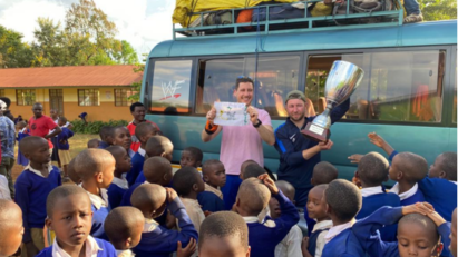 Tanzanian school children greeting two members of FC Cambounet outside their school.