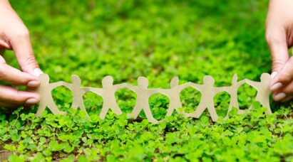 A person holding a paper chain family on a bed of grass.