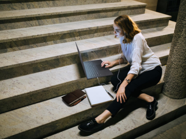 A woman casually sitting down on the stairs while working with her LG gram and a notebook.