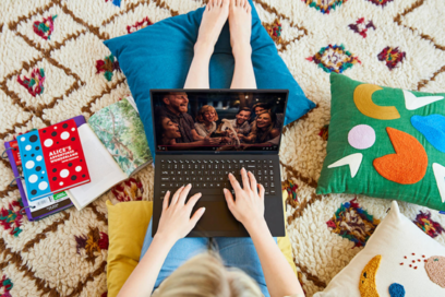 A woman sitting comfortably on the floor with colorful cushions as she watches a TV show on her LG gram.