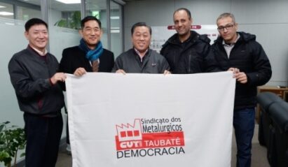 Five men posing with the Steel Workers' Union of Taubate flag.