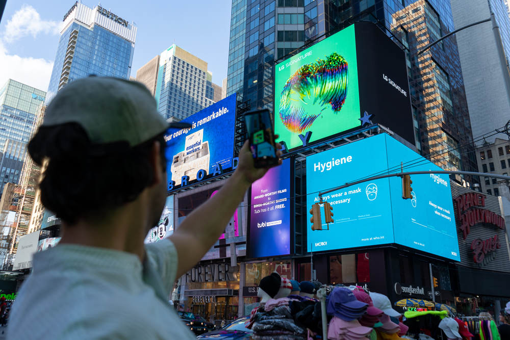 A passerby taking a picture of LG's massive, high-definition digital billboard in Time Square, New York displaying the artwork of David McLeod