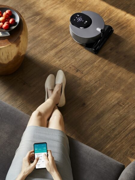 A woman sitting on a sofa as she uses the LG ThinQ app on her smartphone to control the robot vacuum cleaner