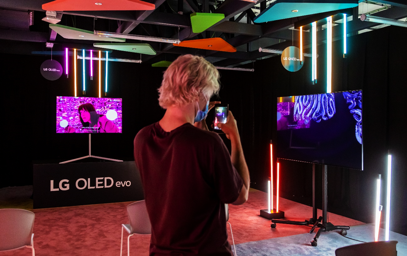 Someone taking a picture of "Deux" by Miguel Checa which is being displayed on LG QNED Mini LED TT with decorative neon lighting surrounding the exhibit