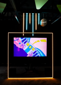 “Fission Fantasy” by Alberto Luango, which depicts the inside of a colorful subway train, displayed on LG NanoCell TV with neon lighting hanging above