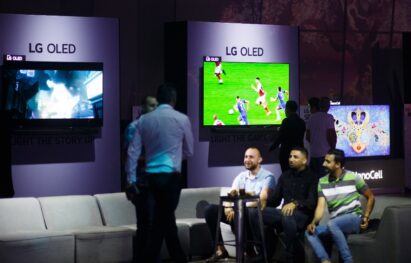 A group of people sitting on a sofa at the LG OLED TV launch in Israel with LG’s TVs displaying content on the wall behind them.
