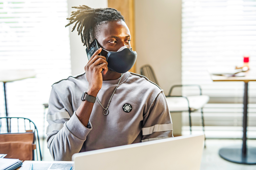 A man using his smartphone without removing LG PuriCare Wearable thanks to the clearness of VoiceOn technology.