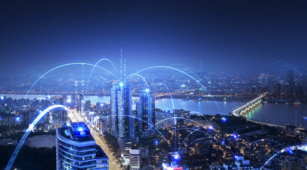 A city skyline at night with buildings connected with blue light to depict telecommunication technology.