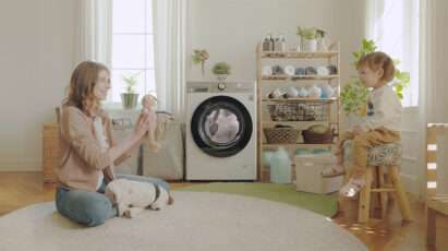 A mom playing with her daughter in the laundry room with LG washer running behind.