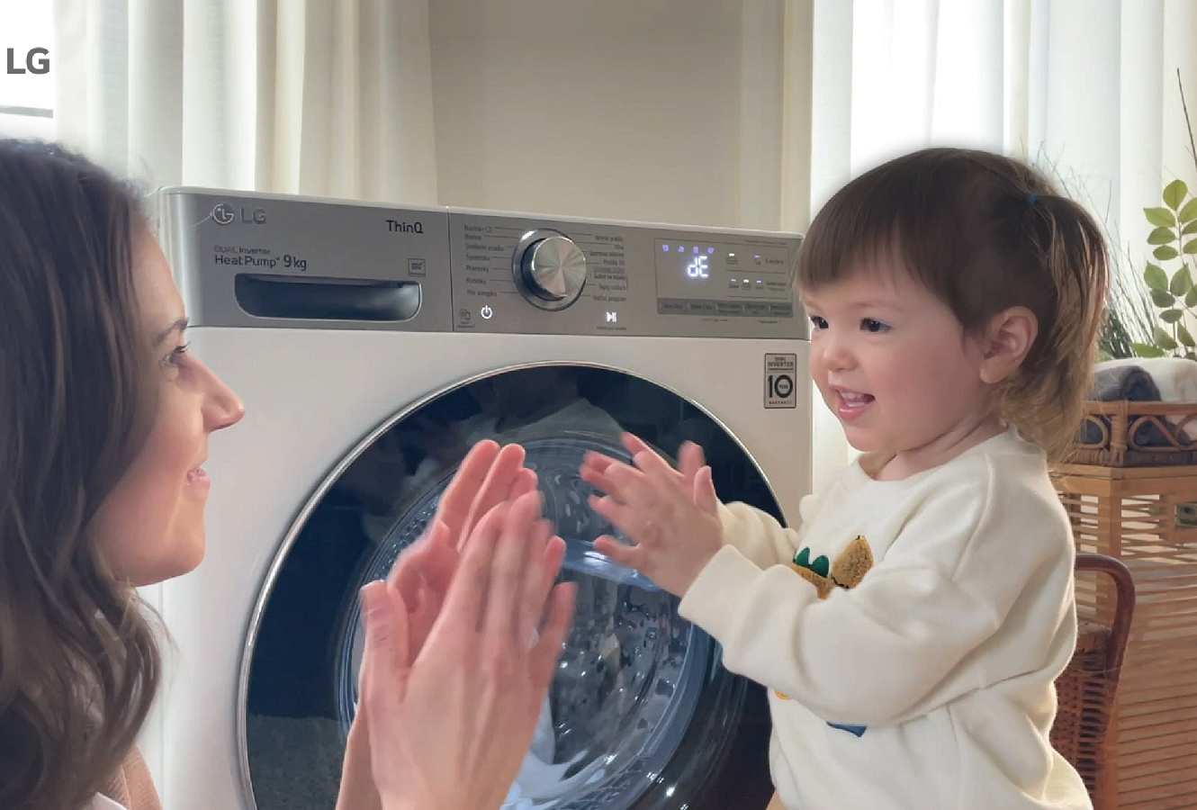 A mom playing with her daughter in the laundry room with LG washer running behind.