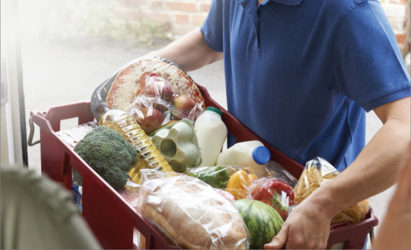 A volunteer delivering a basket of fruits, vegetables and milk to a home in need.