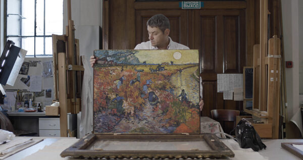 A restoration expert removing “The Red Vineyards at Arles” painting from its frame. 