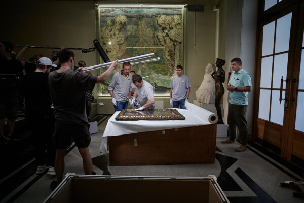 A film crew capturing the restoration process of removing the historic painting from its frame. 
