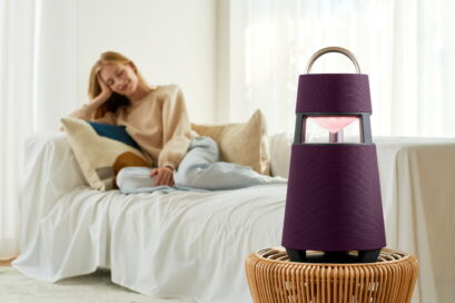 A woman relaxing on the sofa of a cozy living room as LG XBOOM 360 blends perfectly into the interior on top a small rattan table