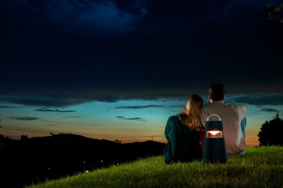 A couple enjoying the sunset on a grass hill with LG XBOOM 360 speaker behind them adding to the calm ambience