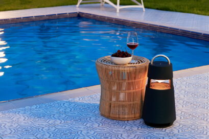 LG XBOOM 360 speaker poolside next to a rattan table with wine and fruit