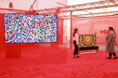 Two visitors discussing the colorful artwork being beautifully displayed on LG OLED TV at an art exhibition with a red theme