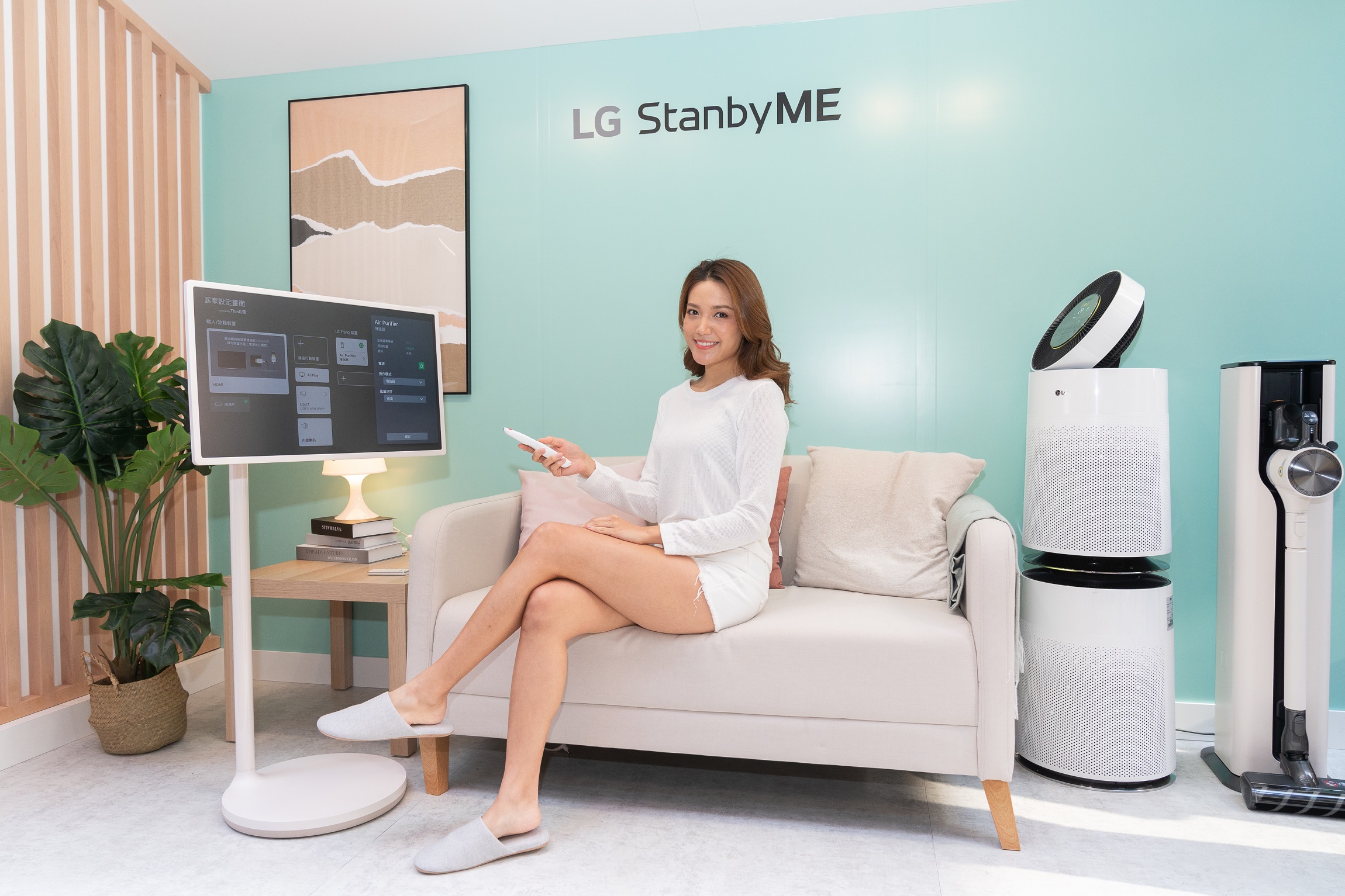 The launch event’s Living Room Zone with a woman using LG StanbyME on the sofa next to LG’s air purifier and CordZero vacuum.