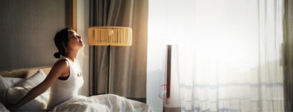 LG PuriCare AeroTower air purifying fan is upgrading its features next to a woman waking up from her bed in the morning