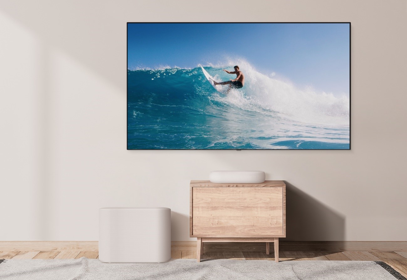 The white LG Éclair and subwoofer placed below a wall-mounted LG TV to effortlessly blend into a simply decorated white room