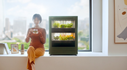 A woman sitting on a large windowsill that looks out on the city as she enjoys a cup of tea next to LG tiiun.