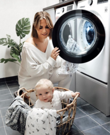 A woman using an LG washing machine to do her laundry as her baby plays inside the clothes basket.
