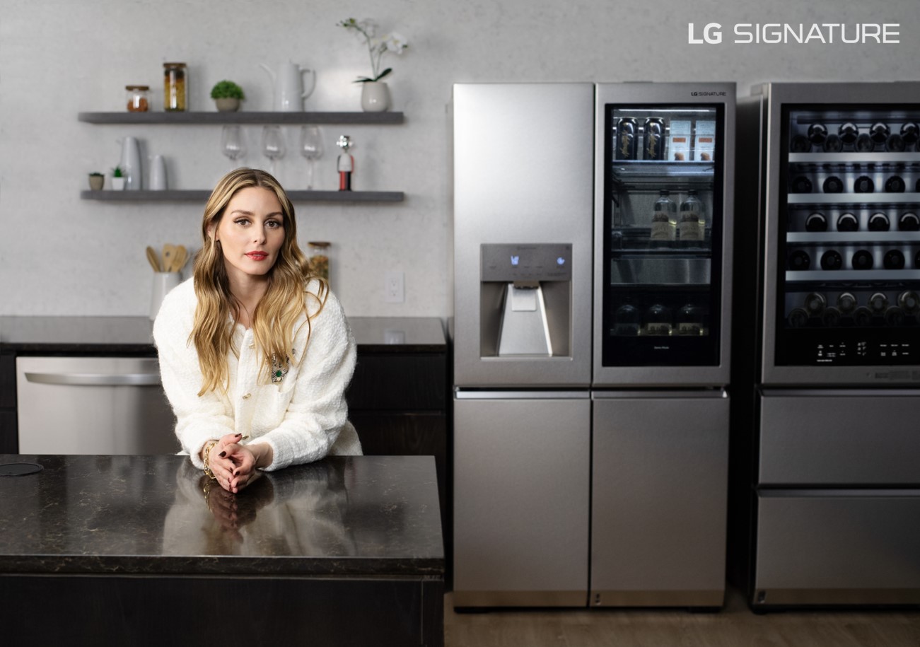 Olivia Palermo is perching over the kitchen counter next to the LG SIGNATURE InstaView™ Door-in-Door® Refrigerator