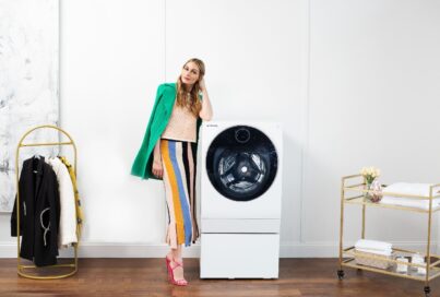 Olivia Palermo is leaning on the LG SIGNATURE Washer/Dryer Combo, positioned between a hanger and laundry trolley.