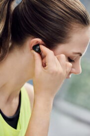 A woman preparing to exercise by placing a LG TONE Free fit earbud in one ear.