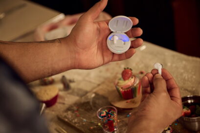 Someone holding LG TONE Free in white on a table surrounded by colorful desserts as they take a break from making cupcakes