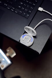 White LG TONE Free earbuds in its case which is plugged into a laptop on a stand.