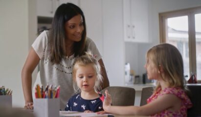 A female talking to kids who are drawing at the dining table