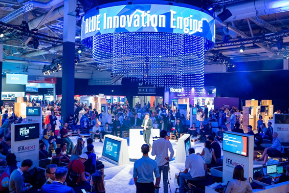 The photo taken during IFA 2022 where many visitors are gathered to listen to the speaker and the phrase "BLUE Innovation Engine" is displayed on a round digital panel