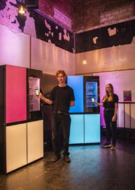 A man and a woman are standing next to the LG MoodUPTM refrigerator changing the color of door panels with the ThinQ app