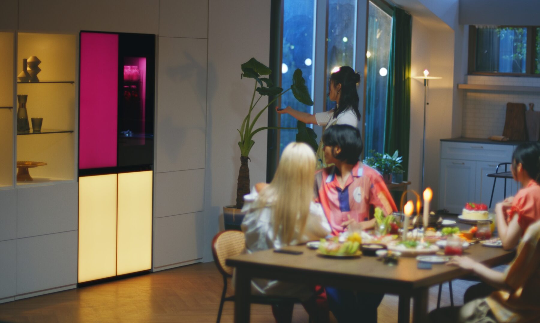 A woman is remotely playing music via a built-in Bluetooth speaker of the LG MoodUP refrigerator at a house party.