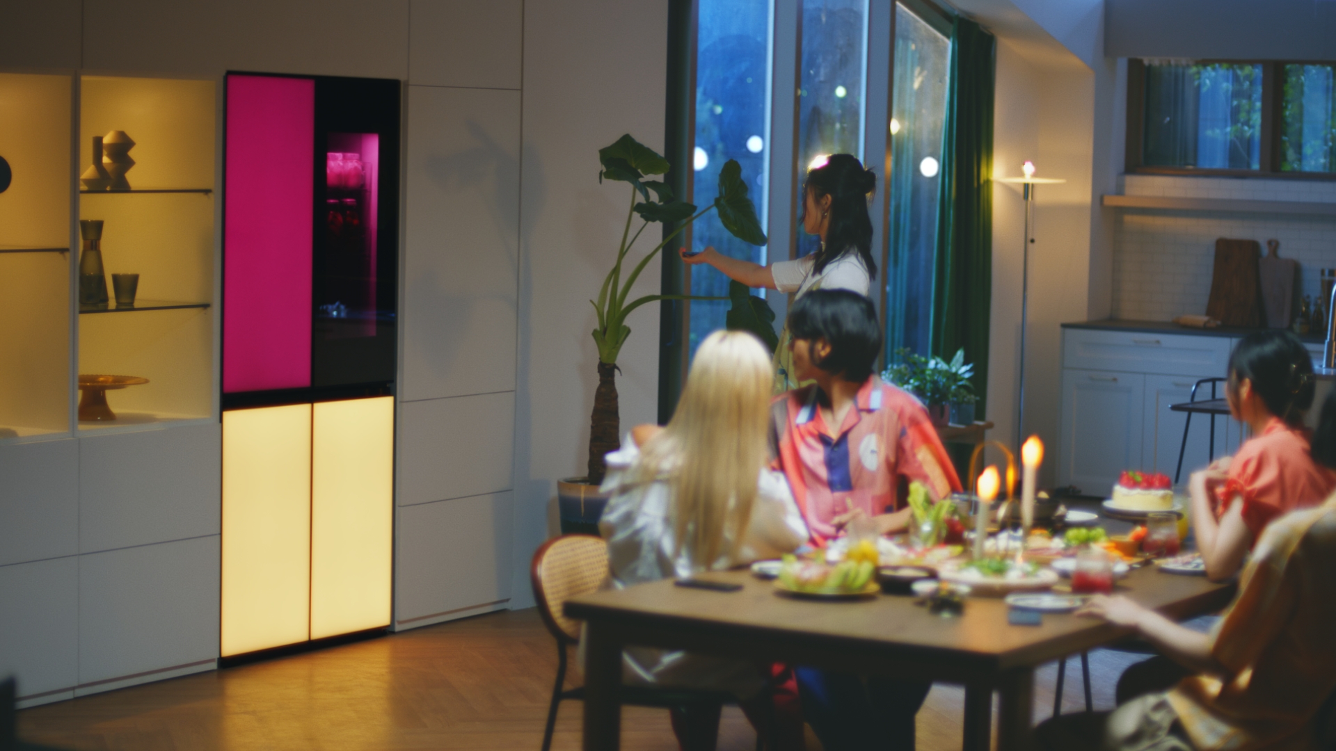 A woman is remotely playing music via a built-in Bluetooth speaker of the LG MoodUPTM refrigerator at the house party