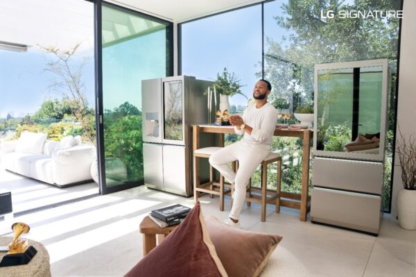 John Legend sitting on a stool between the LG SIGNATURE InstaView Door-in-Door refrigerator and LG SIGNATURE Wine Cellar
