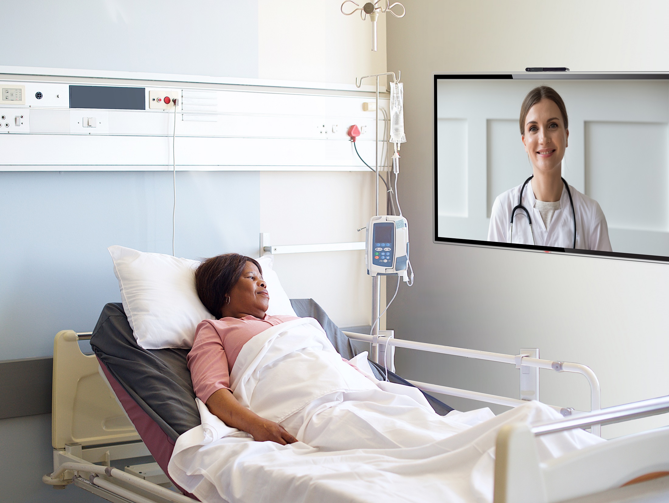 A patient who is resting in a bed is having a video chat with her doctor with the help of LG healthcare TV installed on the wall.