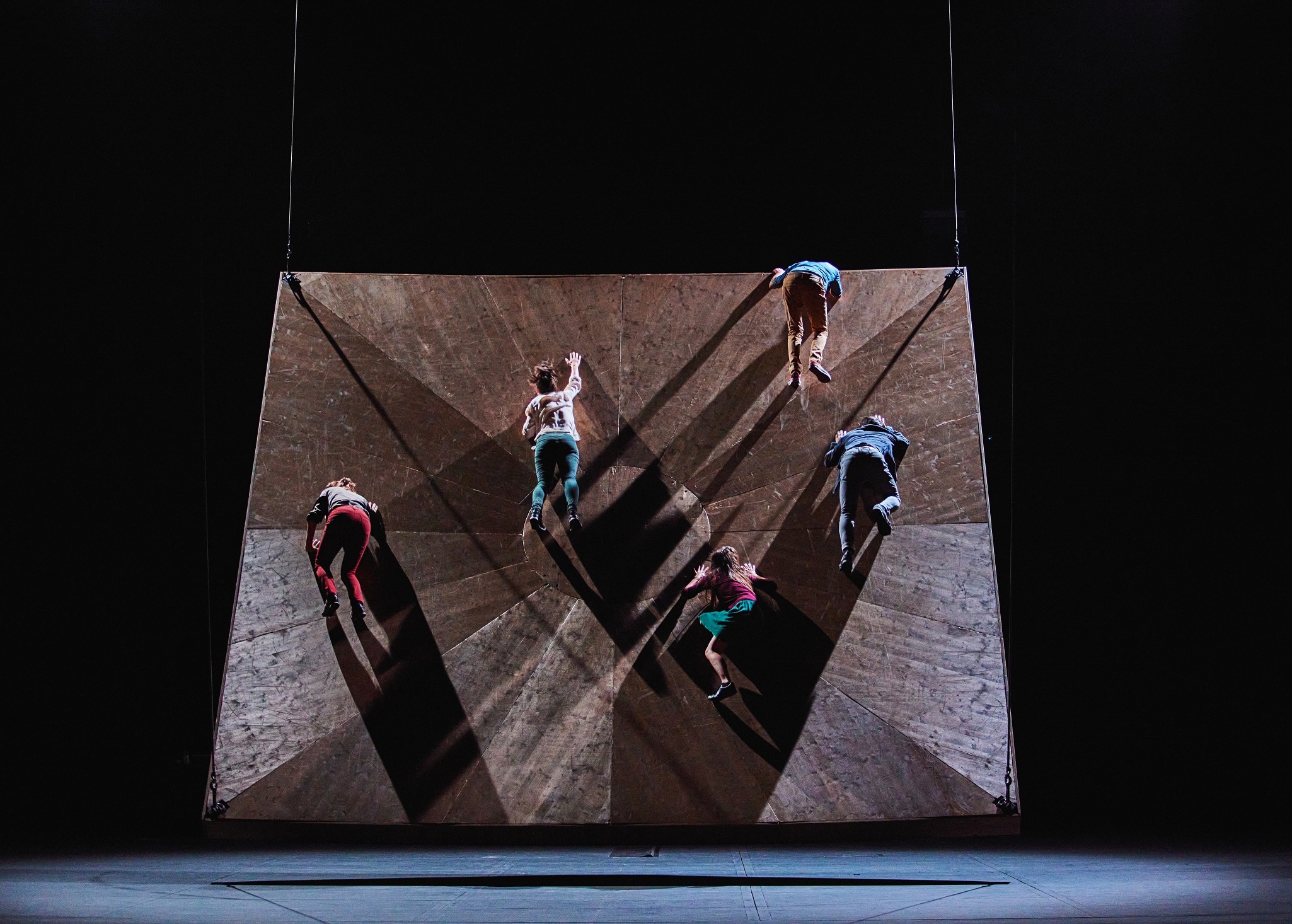 Dancers of the National Choreographic Center of Grenoble balancing on a rectangular platform hanging in the air during the He Who Falls performance