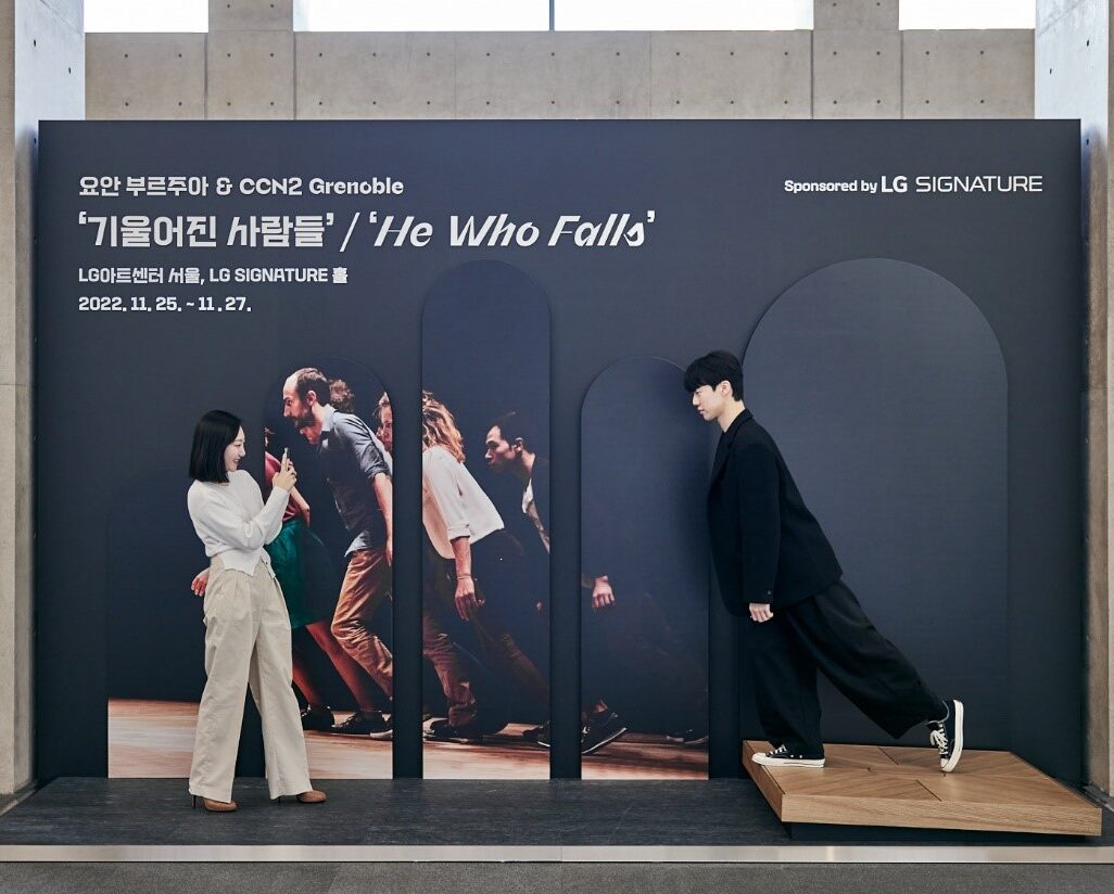 A man posing in front of the He Who Falls photo zone in the LG SIGNATURE Hall as a woman takes a photo