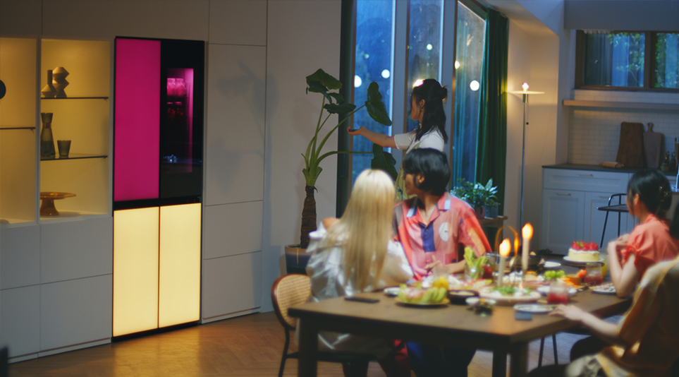 A woman is remotely playing music via a built-in Bluetooth speaker of the LG MoodUPTM refrigerator at the house party